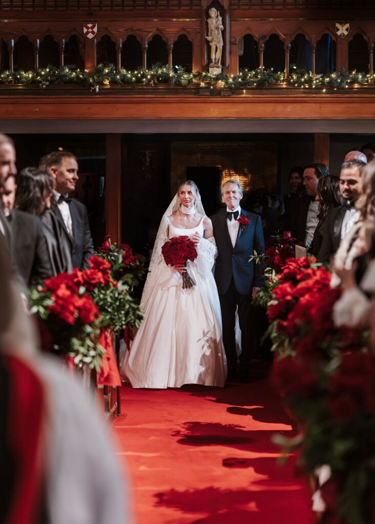 Bride and Dad walking down the aisle surrounded by red roses